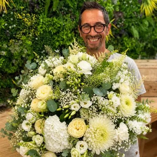 Le fleuriste de la boutique, un grand bouquet de fleurs blanches dans les bras