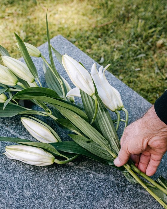Main déposant des lys blancs sur une tombe en granit